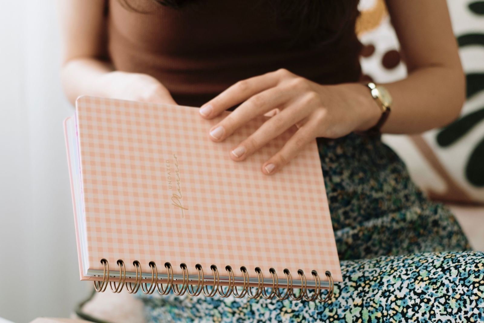 A person holds a pink checkered spiral notebook on their lap