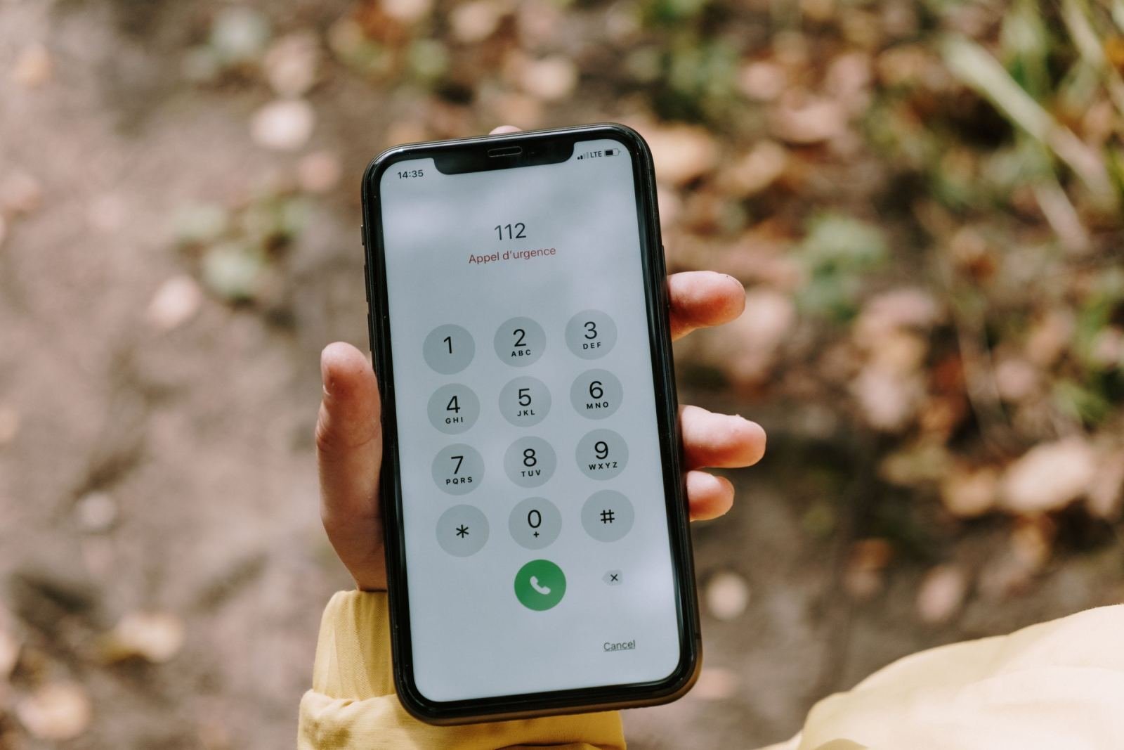 A hand holding a smartphone dialing an emergency number outdoors