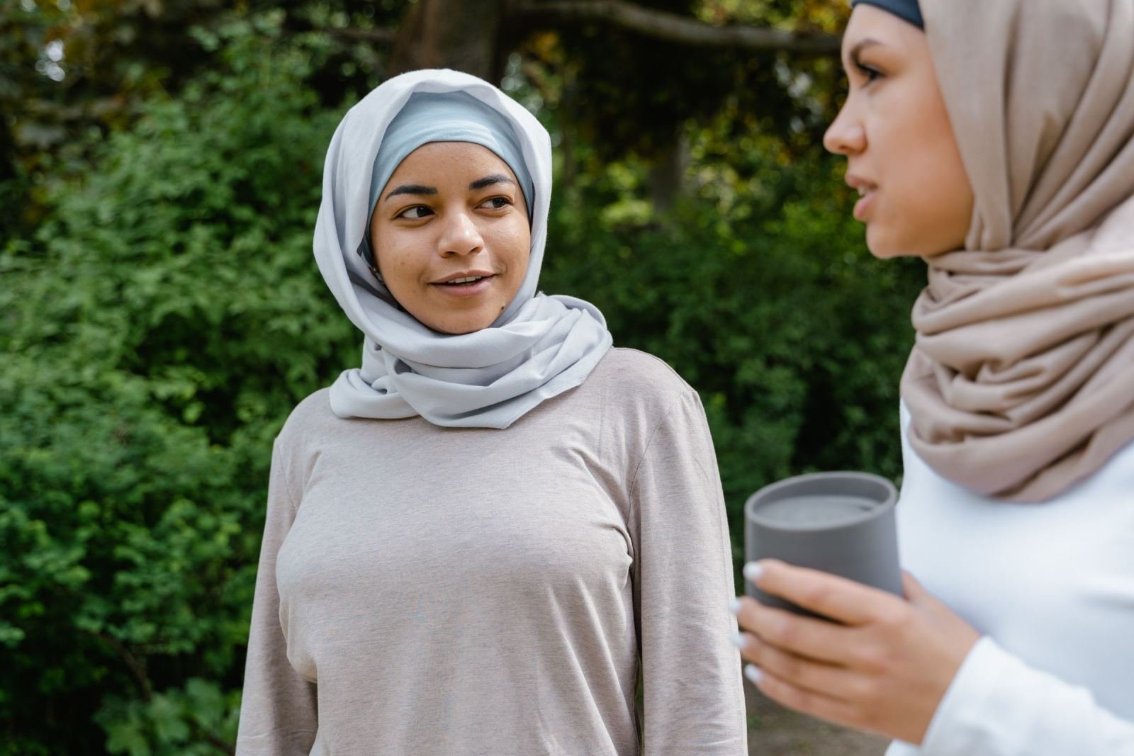 Two women wearing hijabs talk together in a green outdoor setting