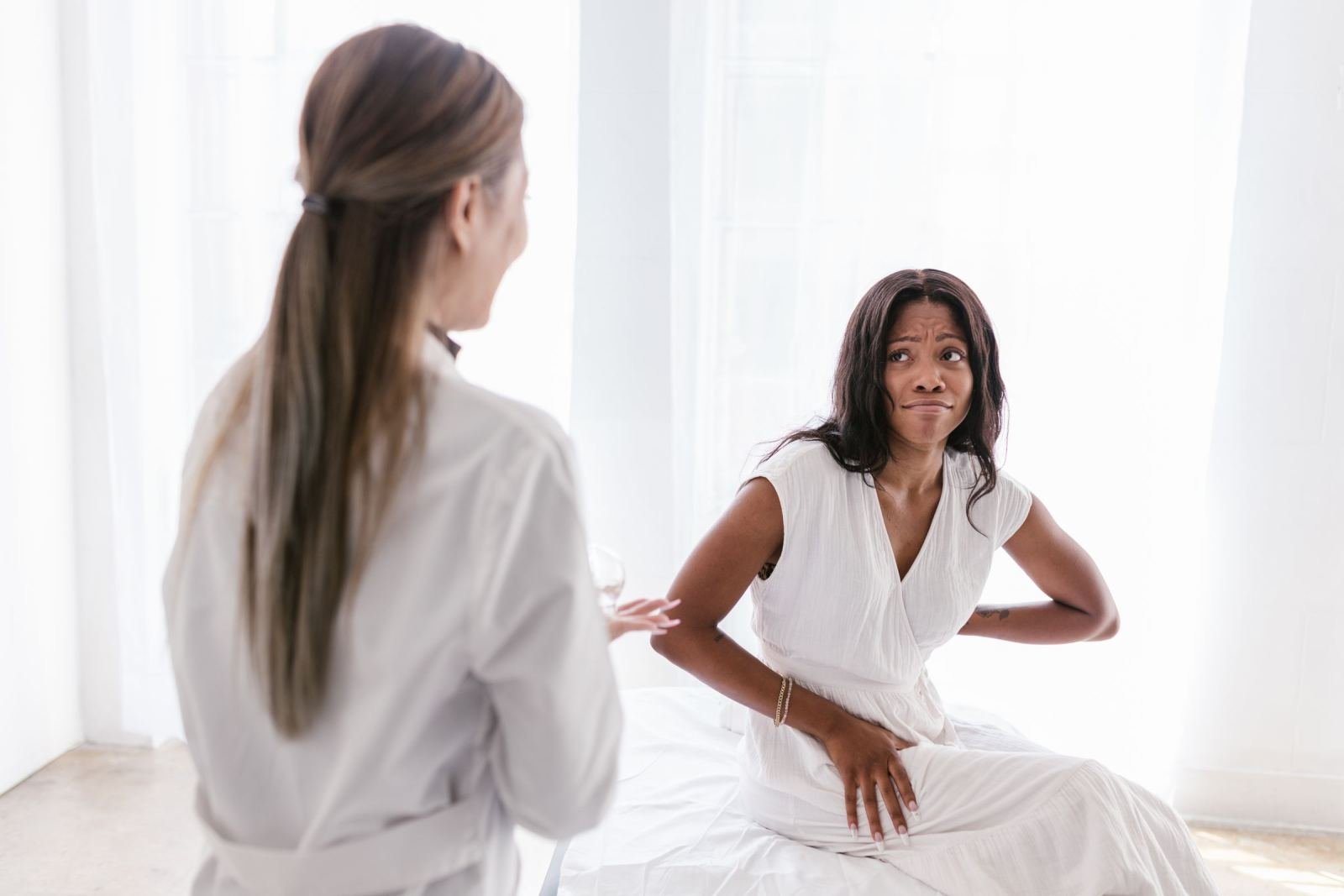 A woman sits in a bright room while a clinician in a white coat speaks with her.