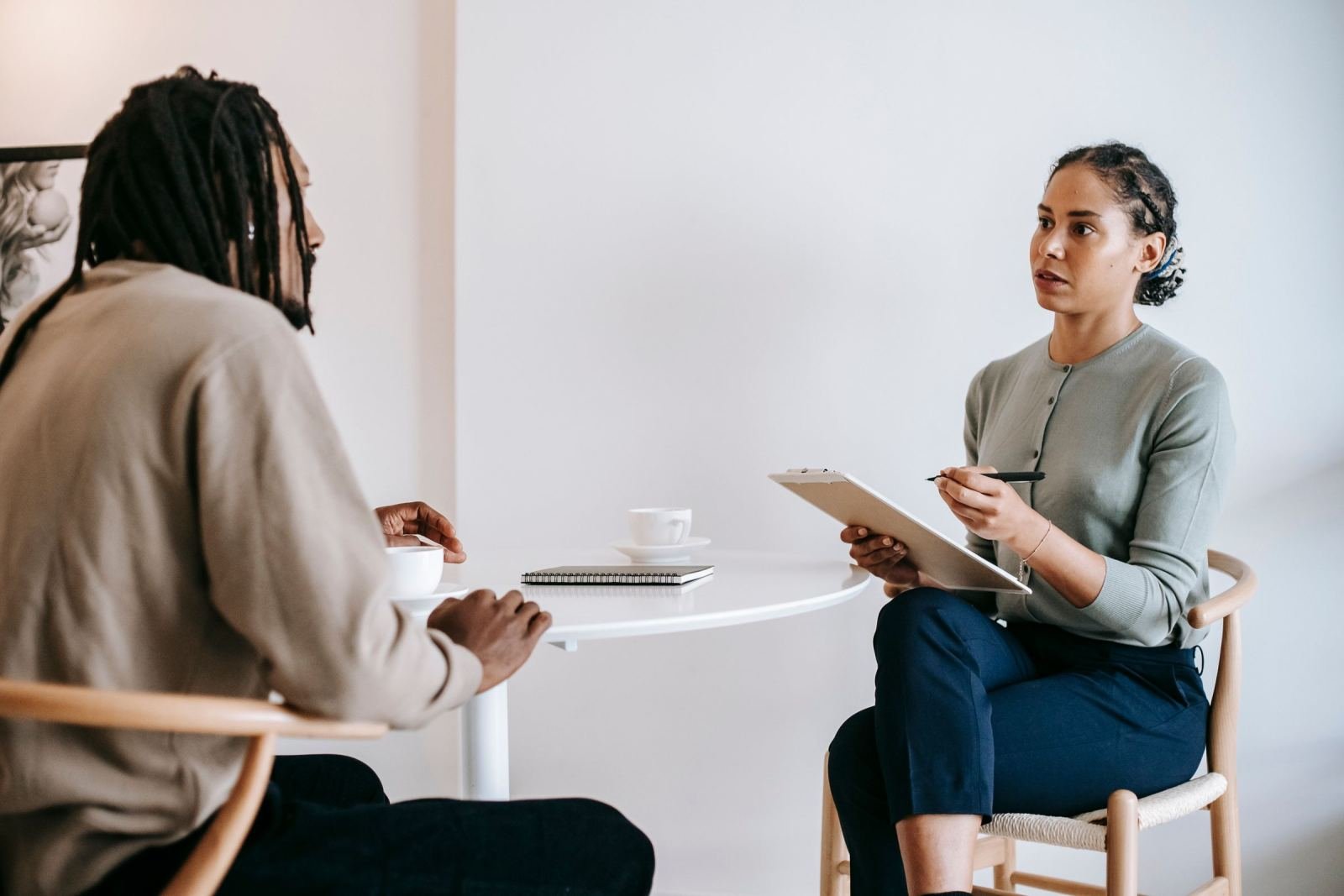A woman with a clipboard talks with a man at a small white table