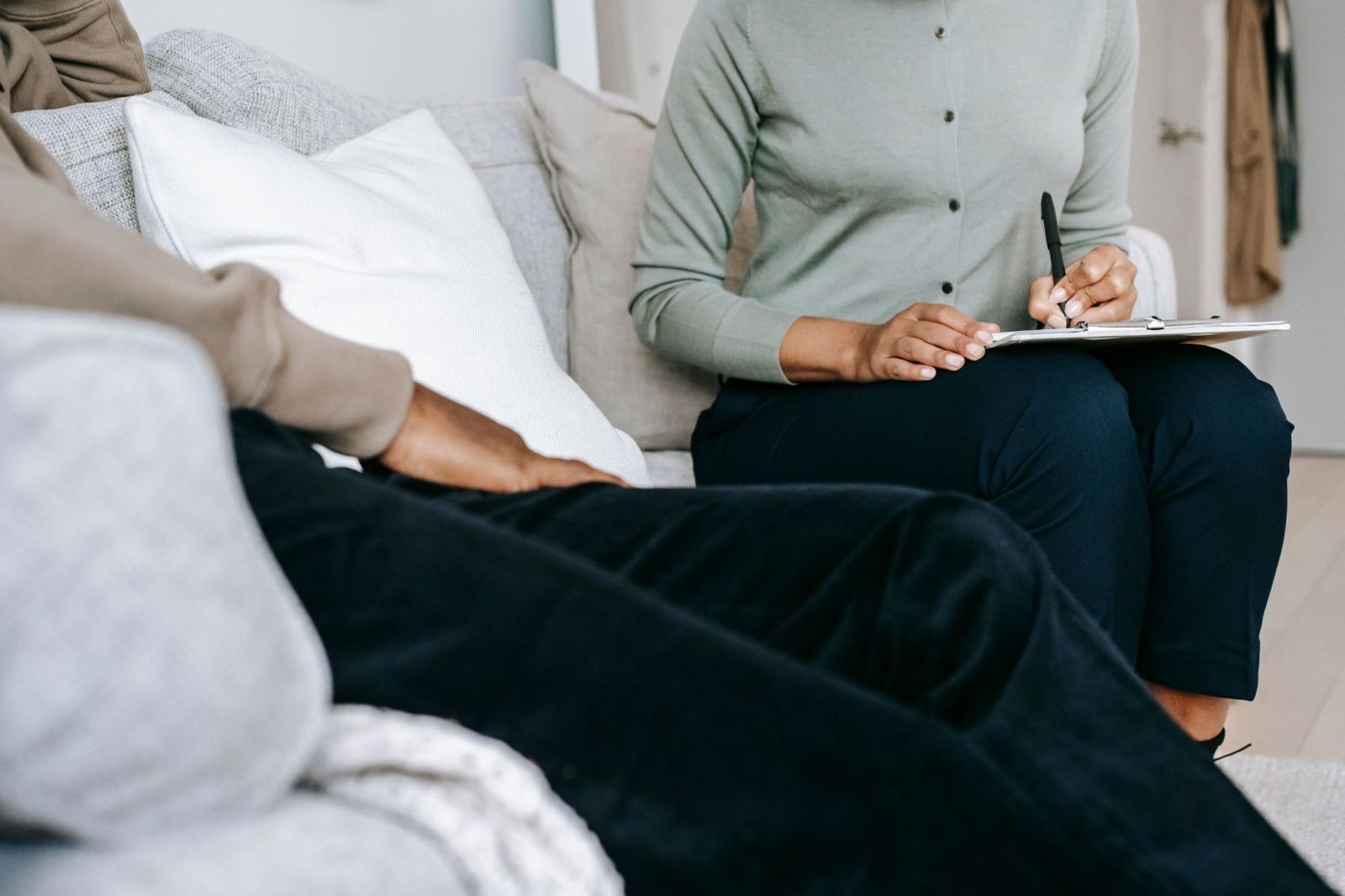 A person in a green shirt takes notes on a clipboard while sitting on a couch with another person