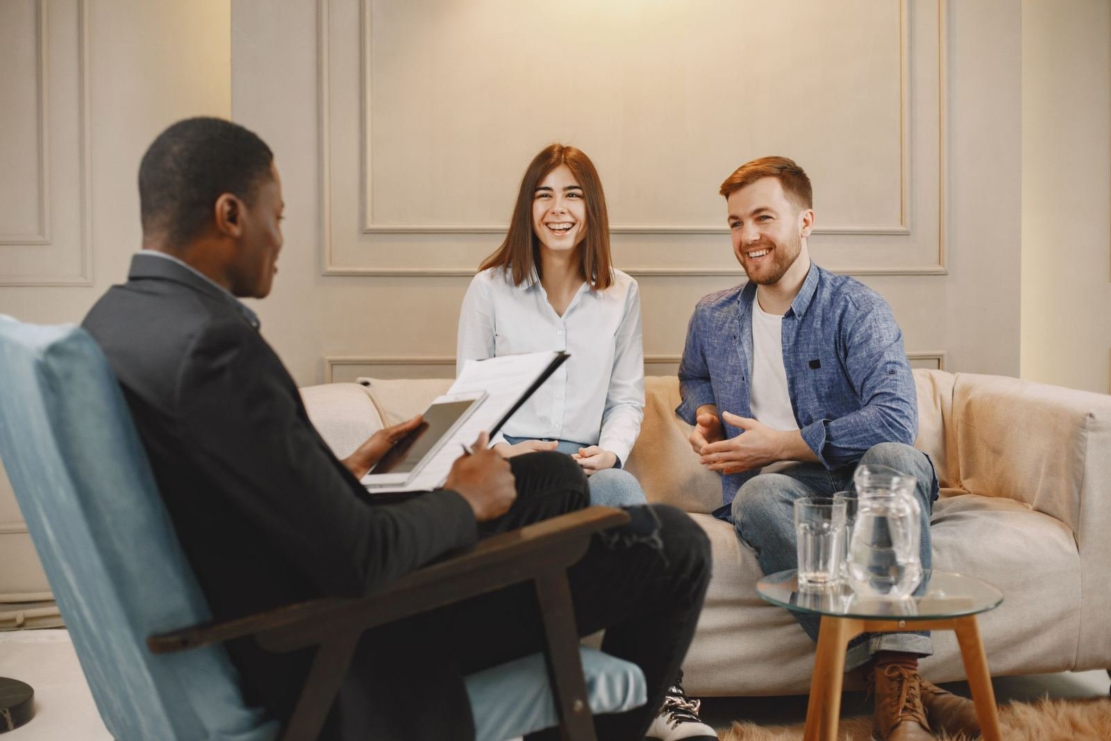 A counselor with a clipboard talks with a smiling couple on a beige sofa