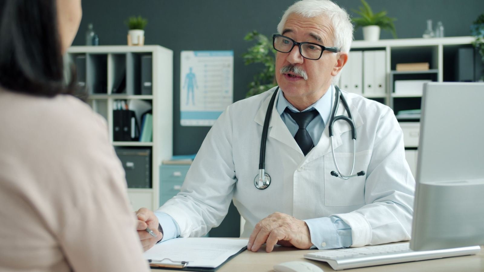 A doctor in a white coat speaks with a patient in a bright office