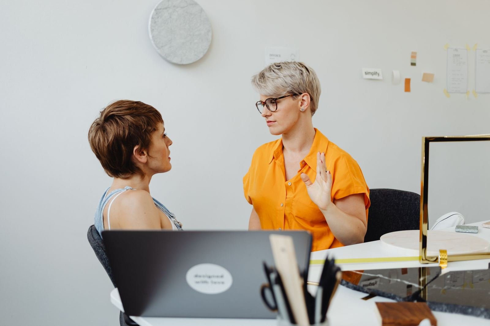 Two women sit at a table talking in a bright office