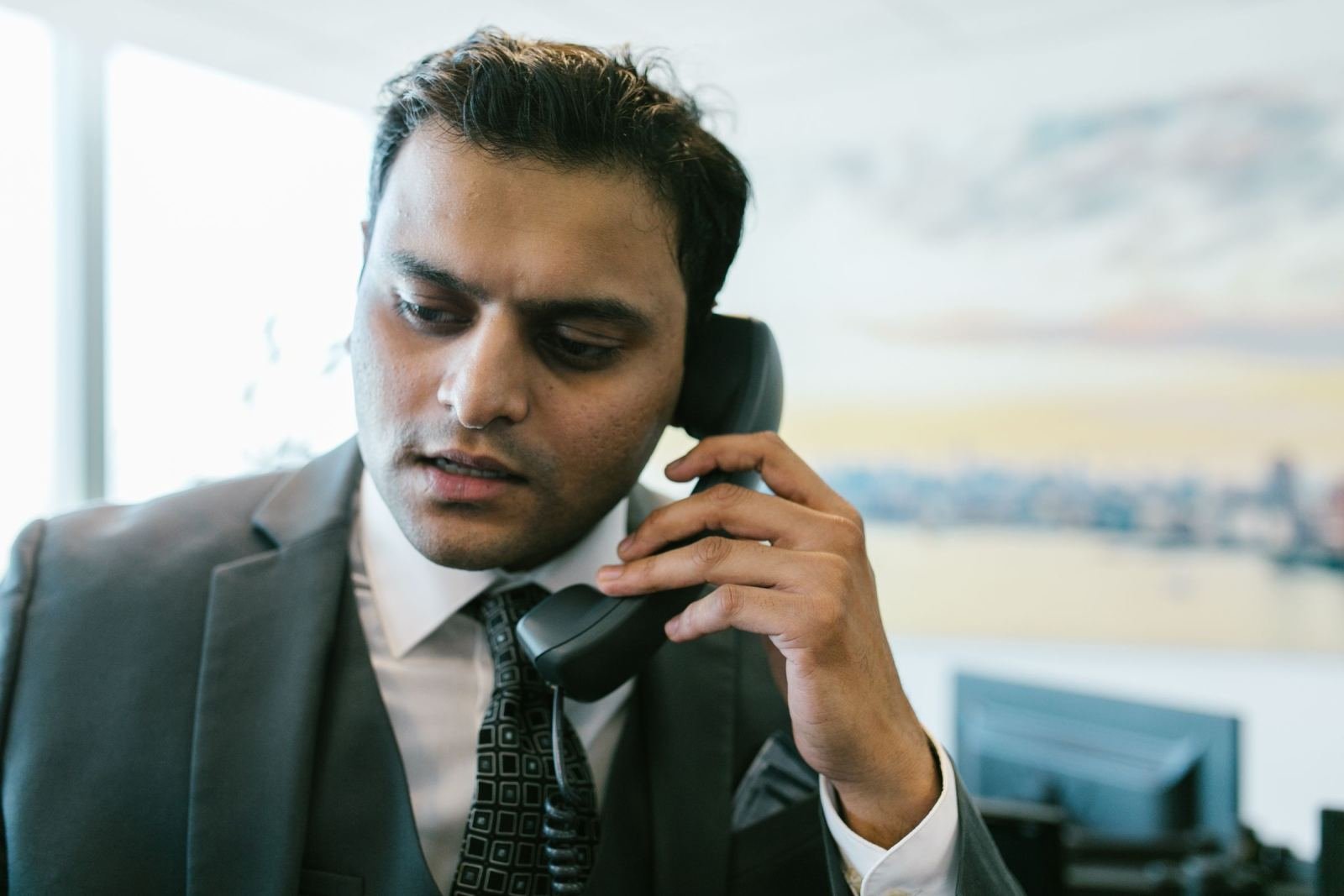 Man in a suit uses a landline phone while sitting in an office