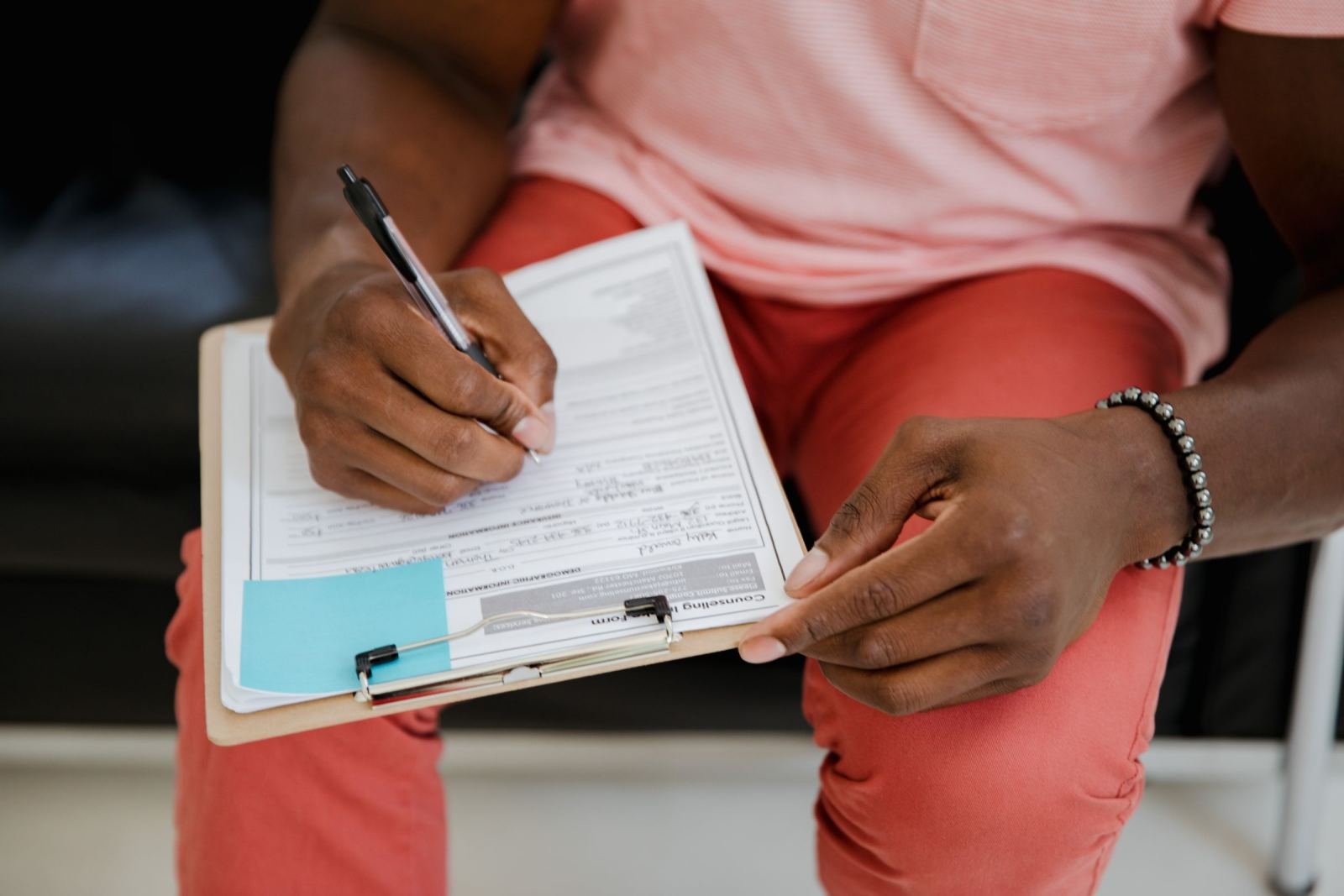 A person writing on a form on a clipboard with a blue sticky note attached