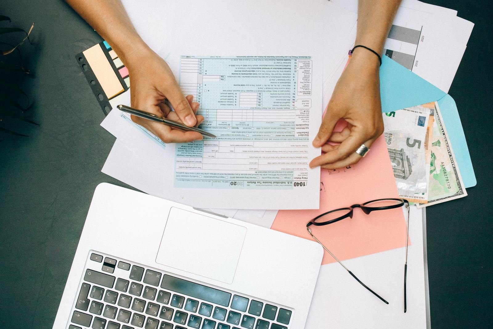 Hands holding a financial document on a desk with a laptop and Euro banknotes