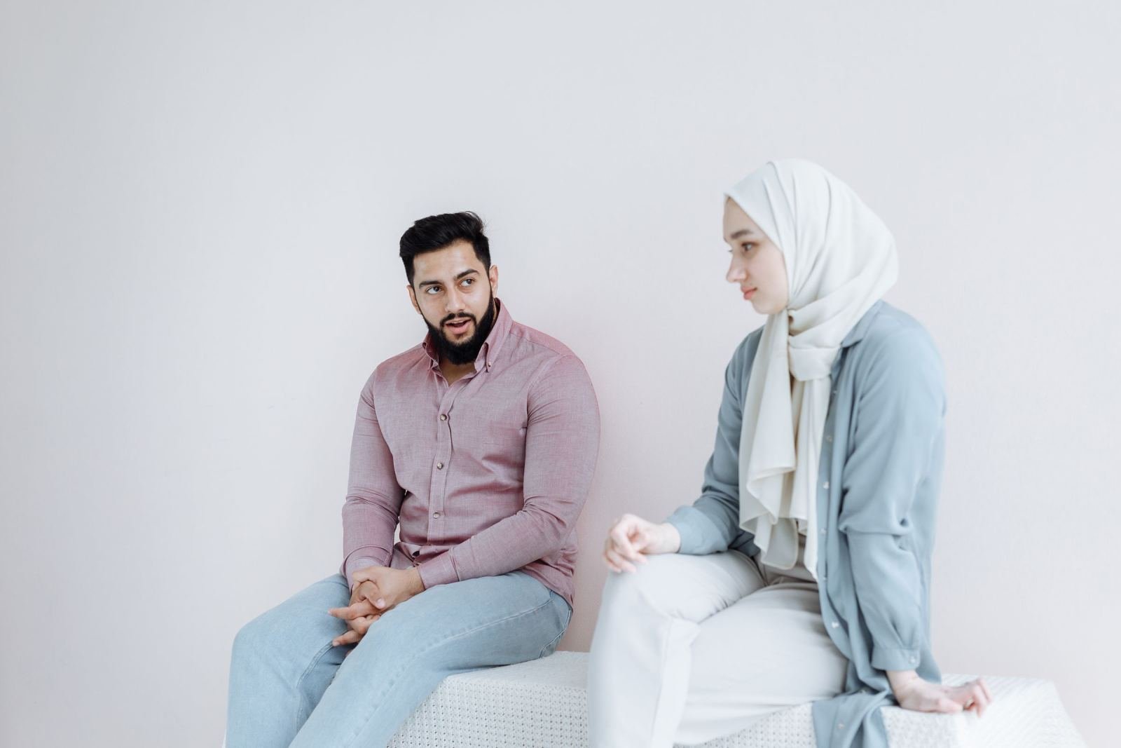 A man and a woman wearing a hijab sit together and talk in a bright room