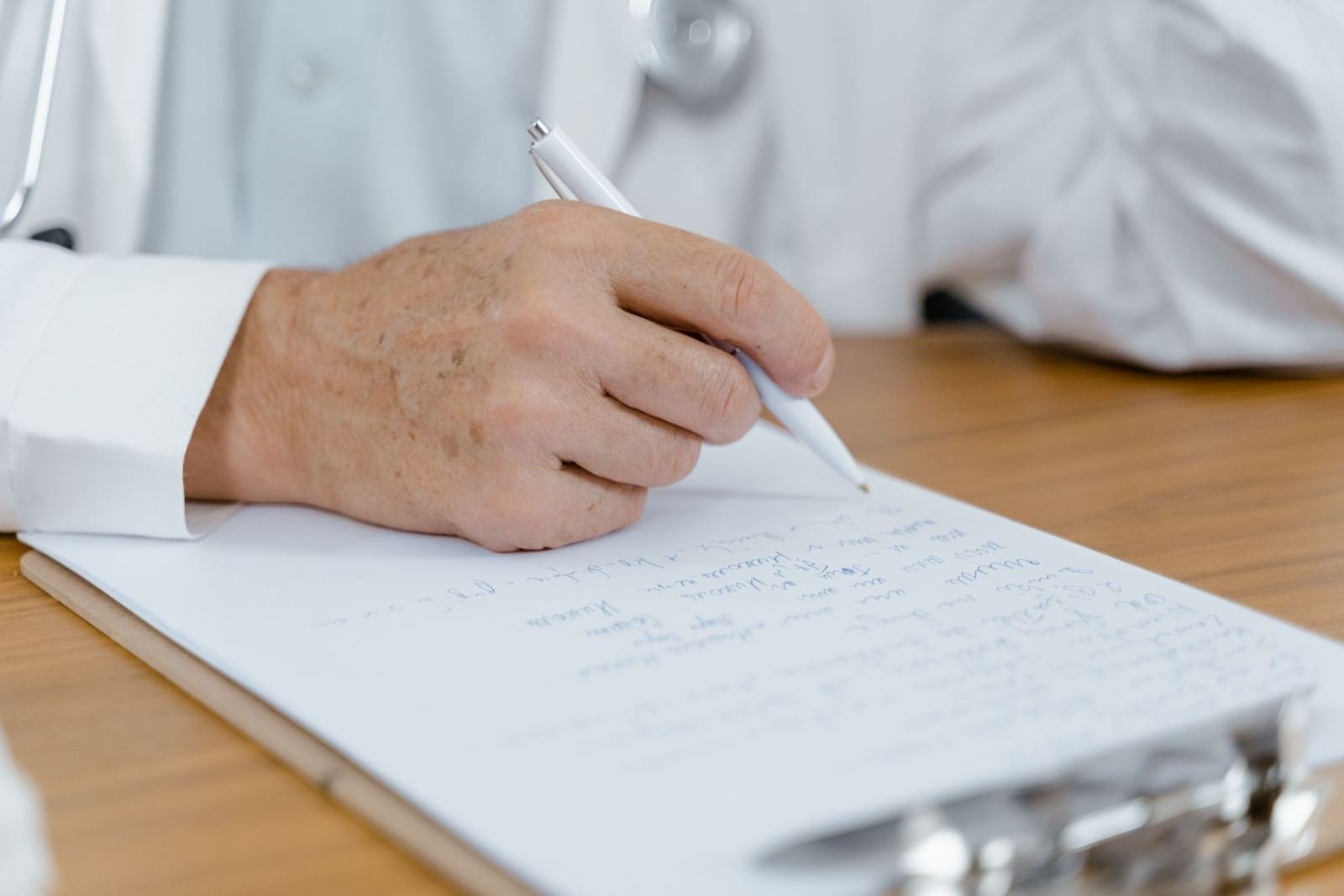 A healthcare provider in a white coat writes notes on a clipboard