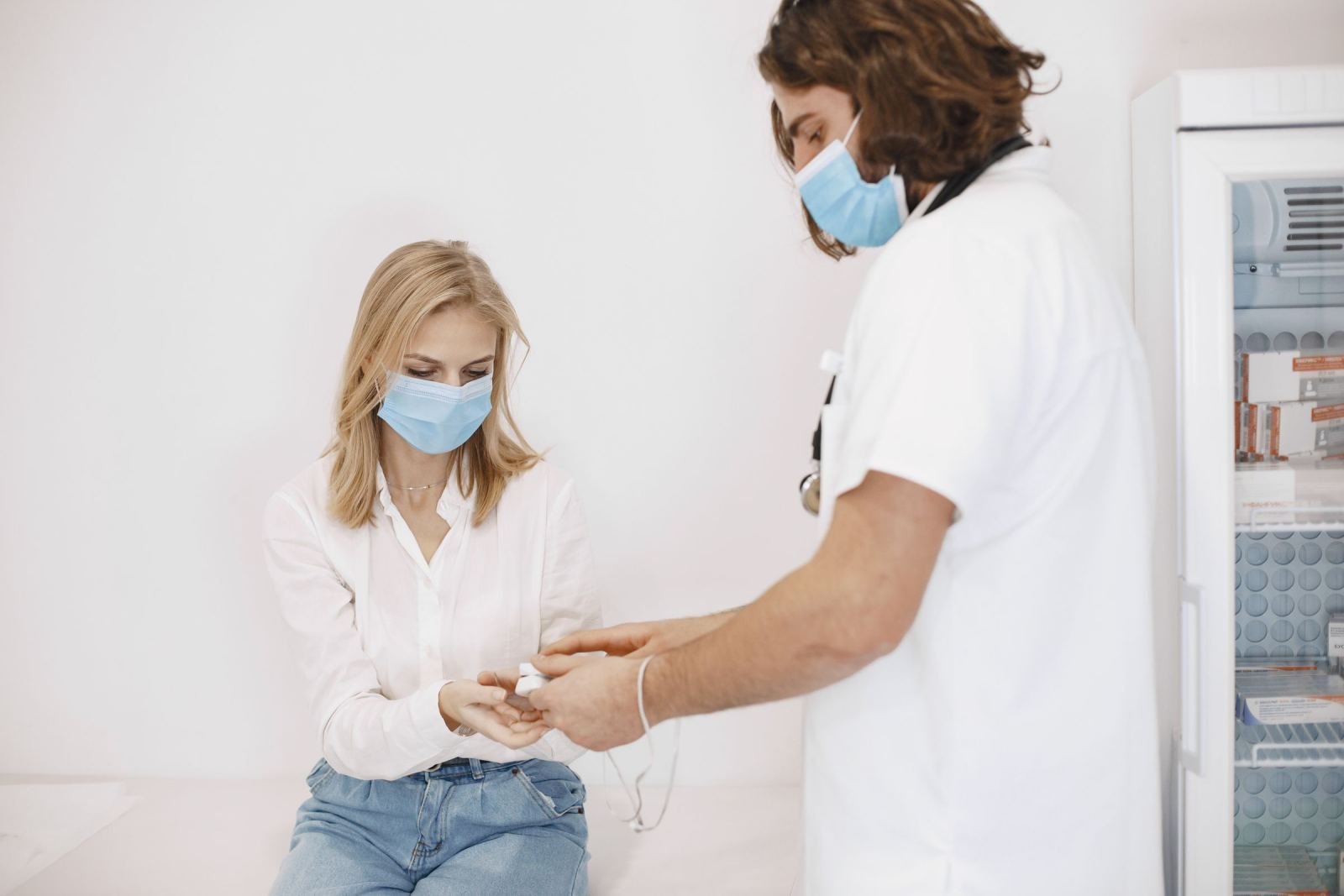 A masked clinician takes a masked patient's pulse.