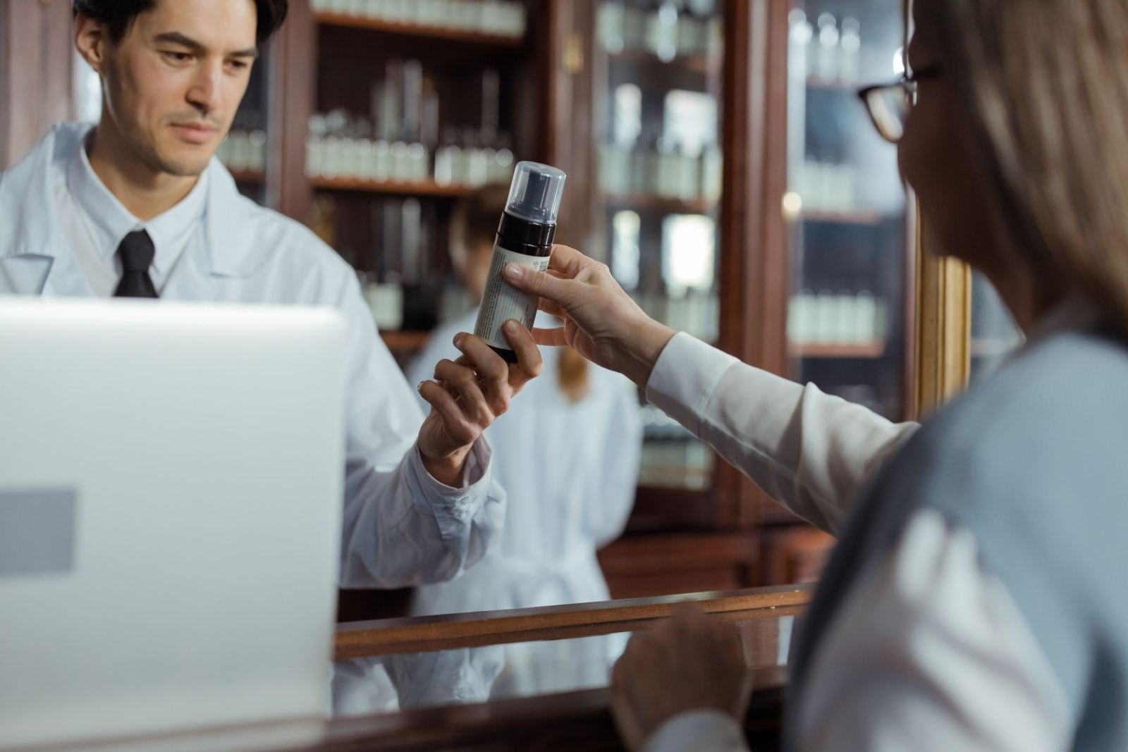 A pharmacist hands a medication canister to a customer across a counter