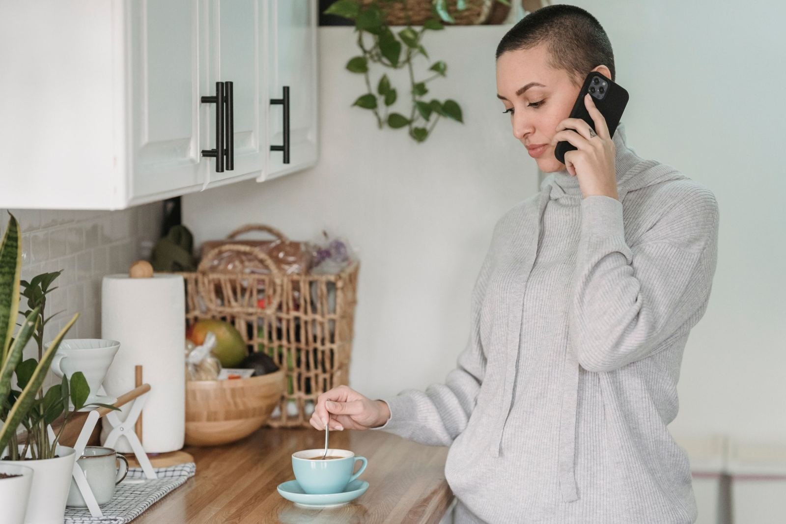 A woman stirs tea in her kitchen while talking on a smartphone
