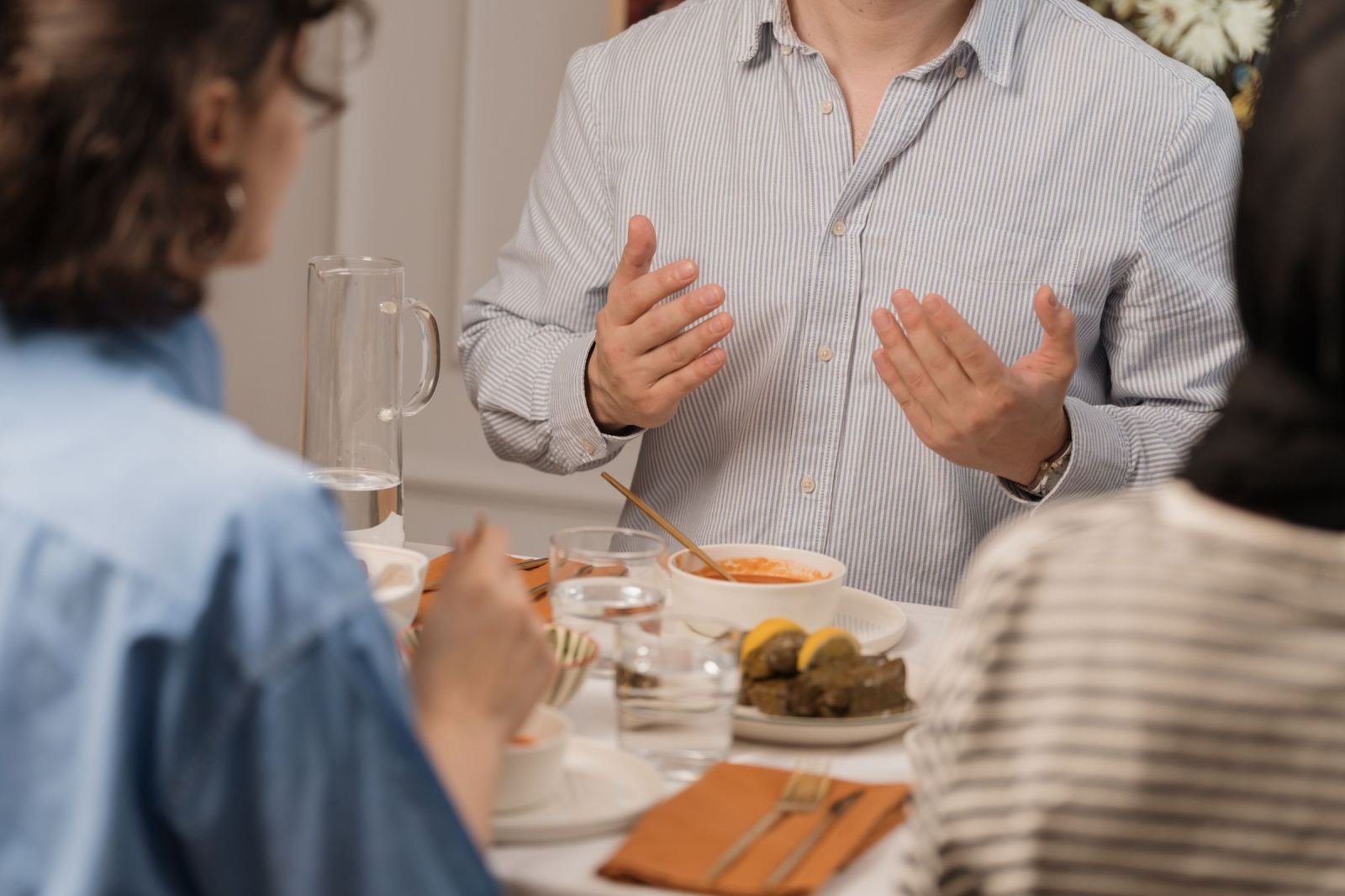 A man gestures with his hands while speaking to others at a dining table
