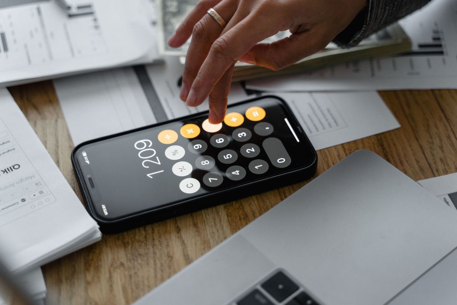 A person using a calculator app on a smartphone next to financial documents