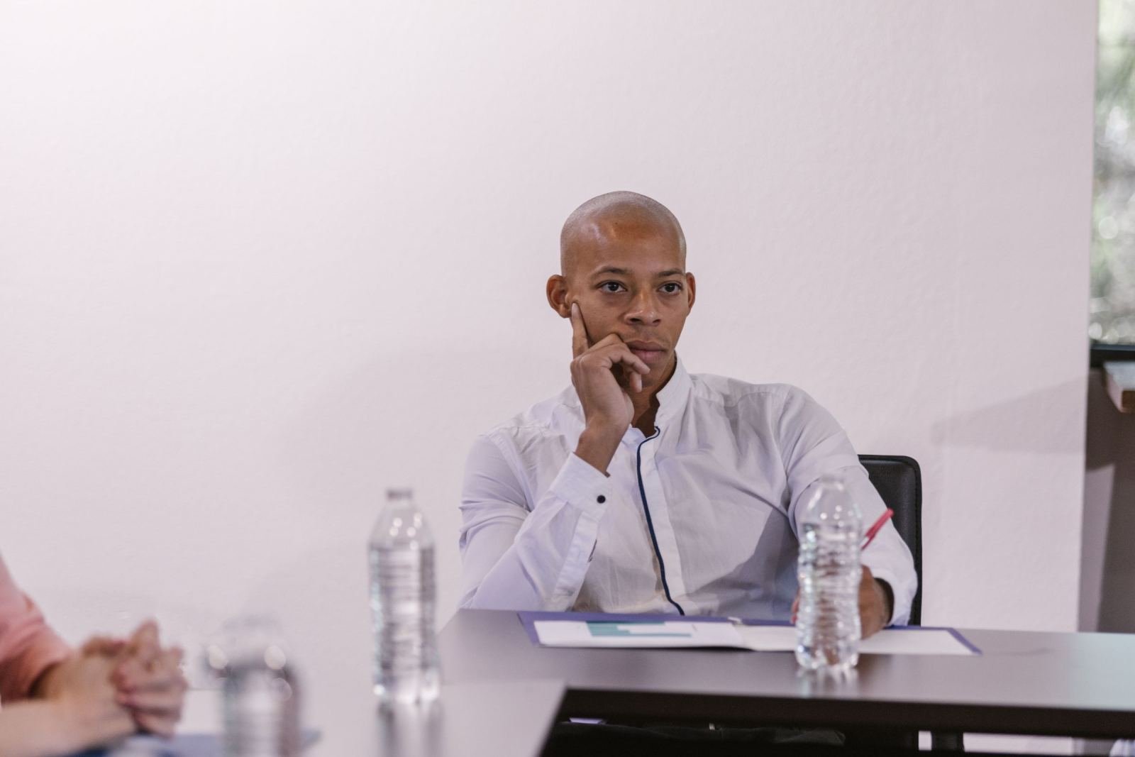 A man in a white shirt sits at a table with water bottles and papers