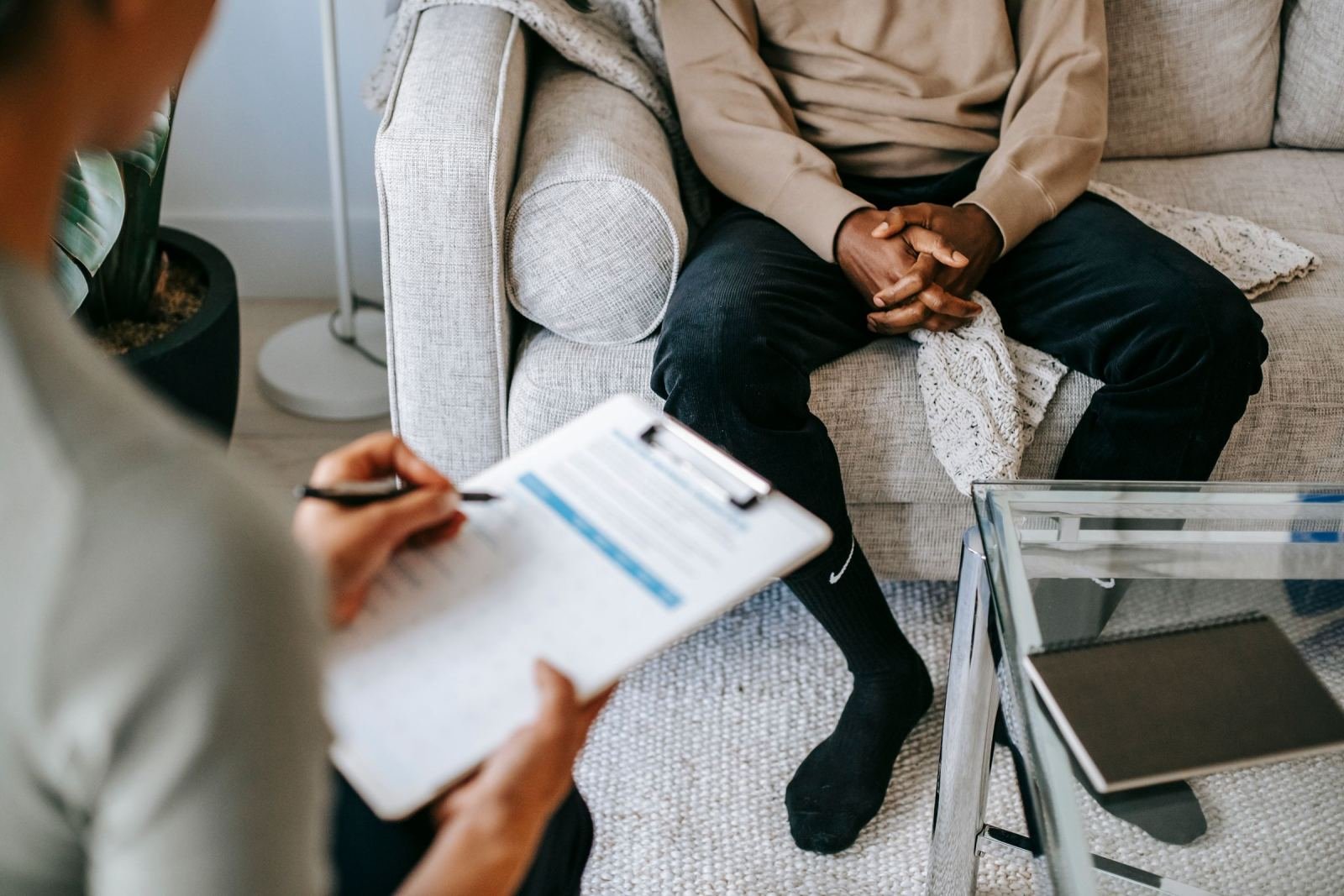 A professional with a clipboard talks to a person sitting on a sofa
