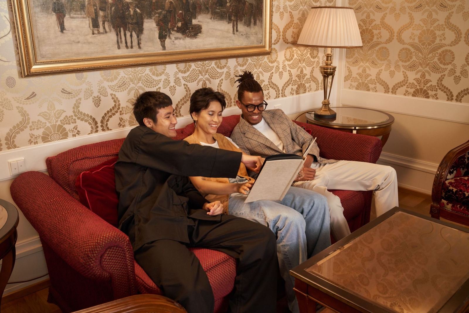 Three people sit on a red sofa looking at a binder together
