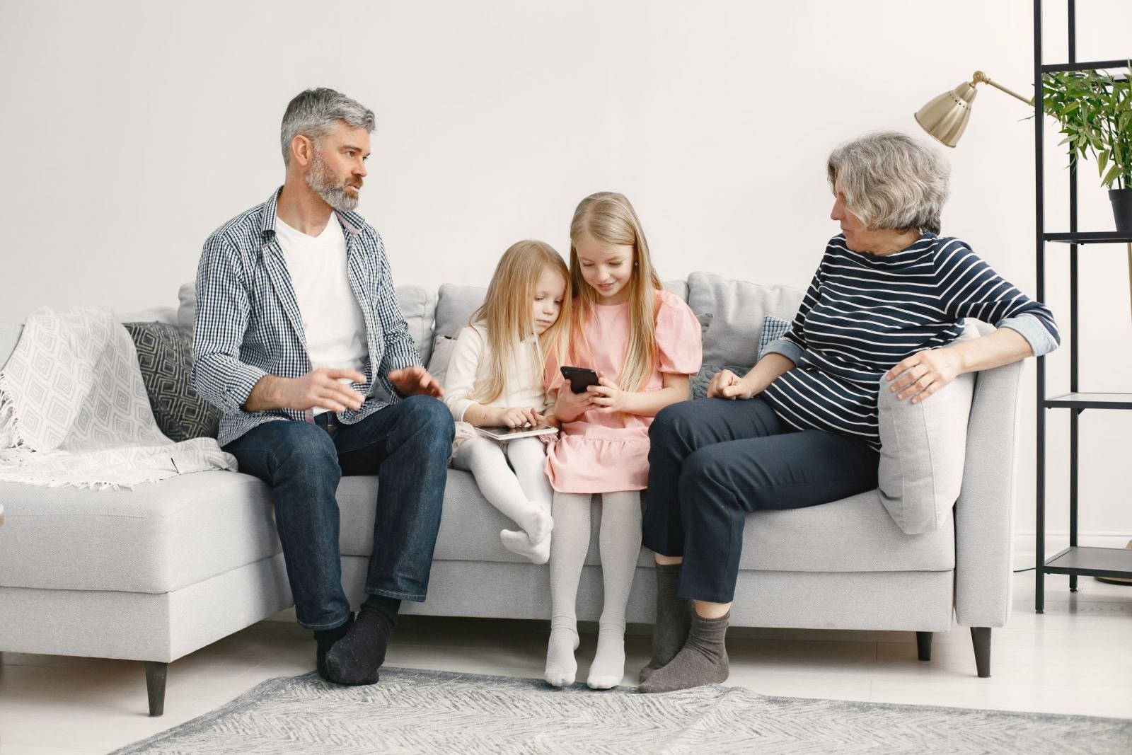 A man, a woman, and two young girls sit and talk on a gray sofa