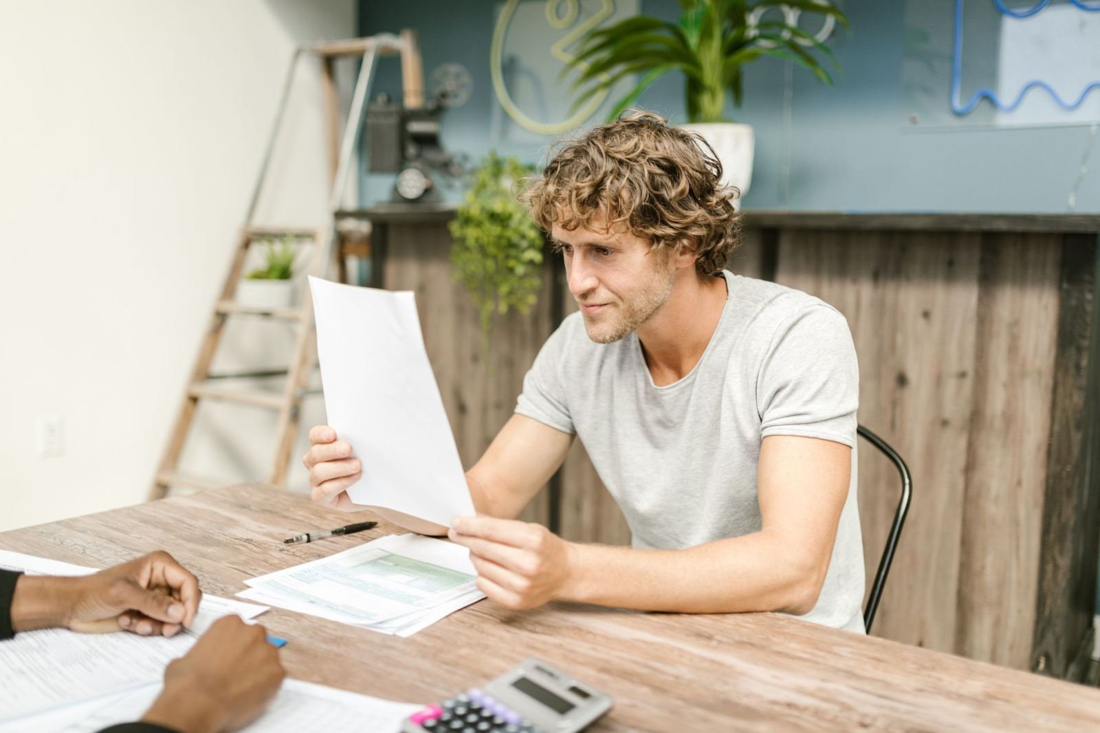 A man reads a document while sitting at a wooden table with another person
