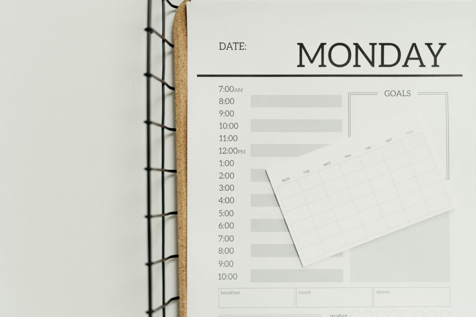 A spiral-bound daily planner page for Monday with a small weekly calendar card on top