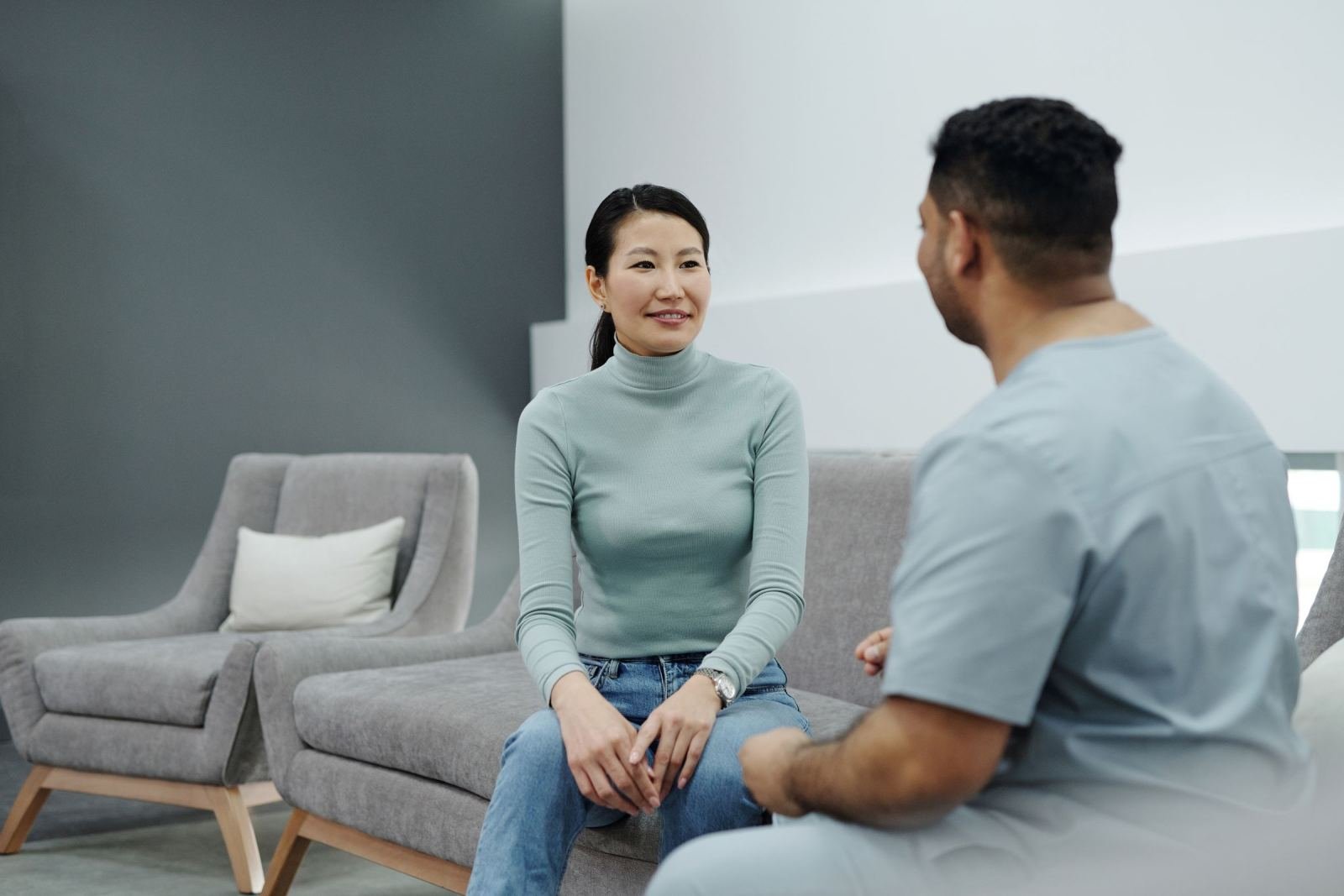 A woman in a green sweater talks with a man in blue scrubs in a modern office