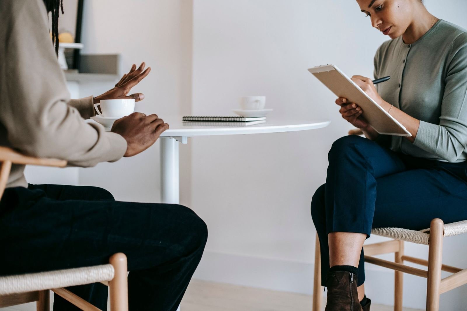 A clinician with a clipboard talks with a man in a bright office