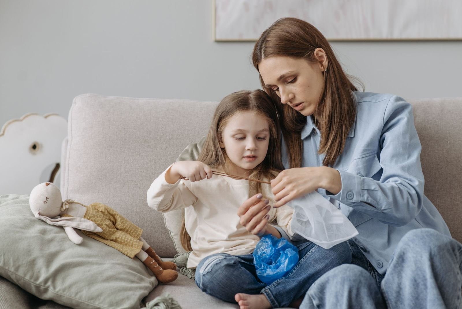 A woman and a young girl sit on a sofa together while working with a piece of fabric
