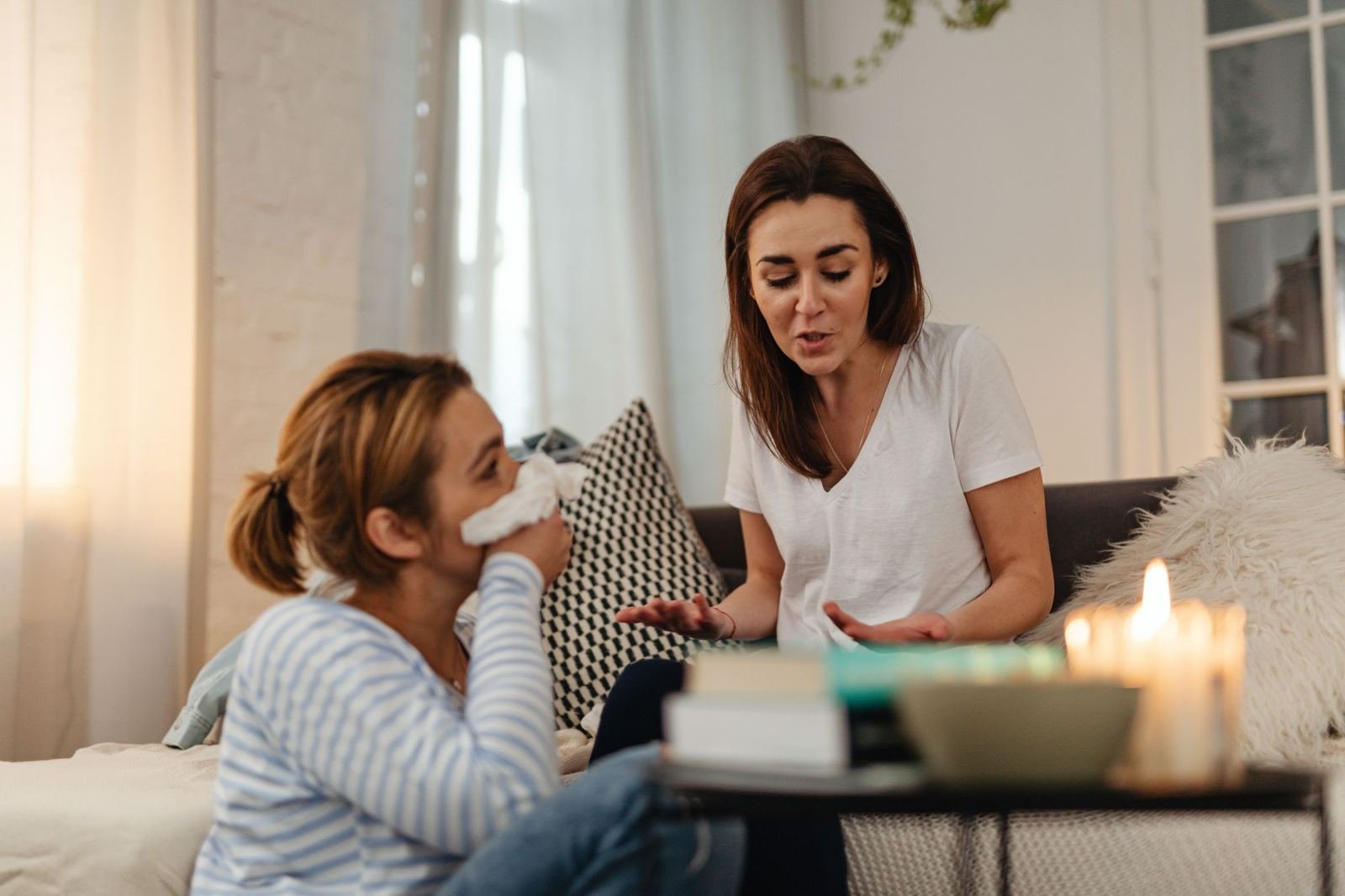 A woman in a white t-shirt speaks supportively to another woman holding a tissue