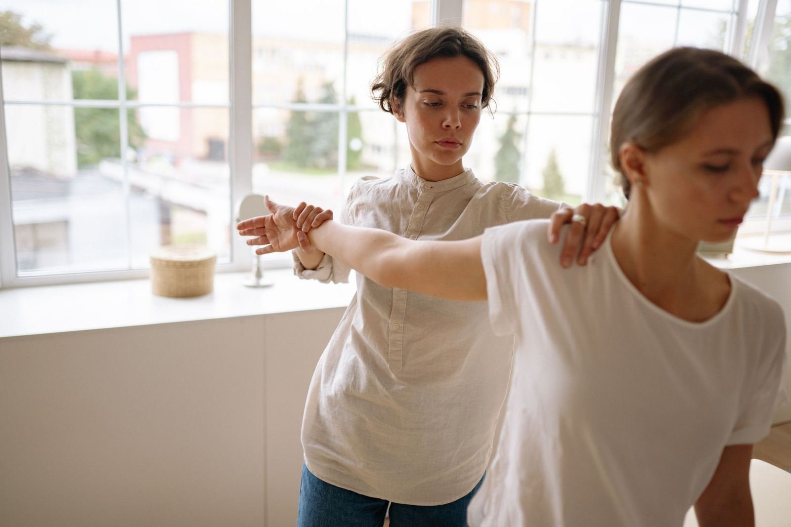 A therapist assists a woman with a stretching exercise in a bright room