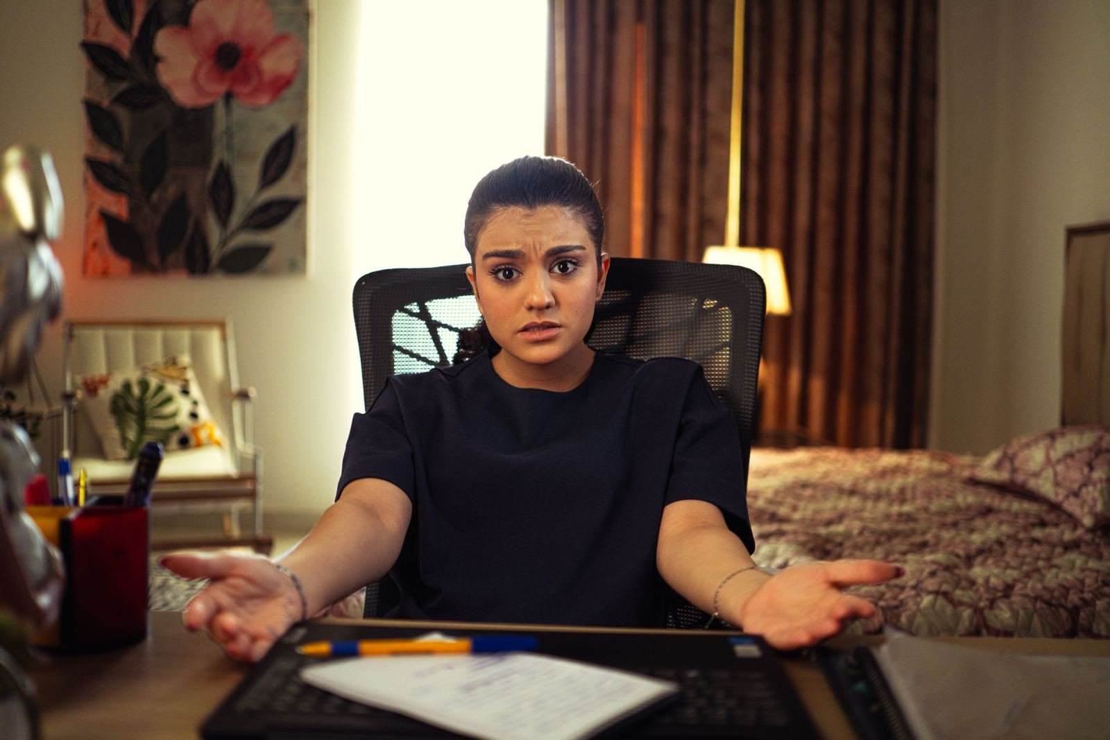 A woman with a confused expression sits at a desk with her hands open
