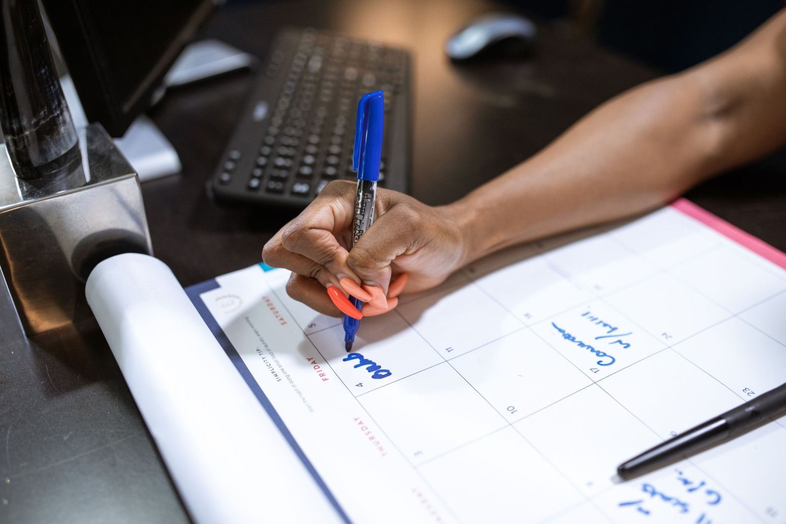 A person writes on a paper weekly calendar at a desk