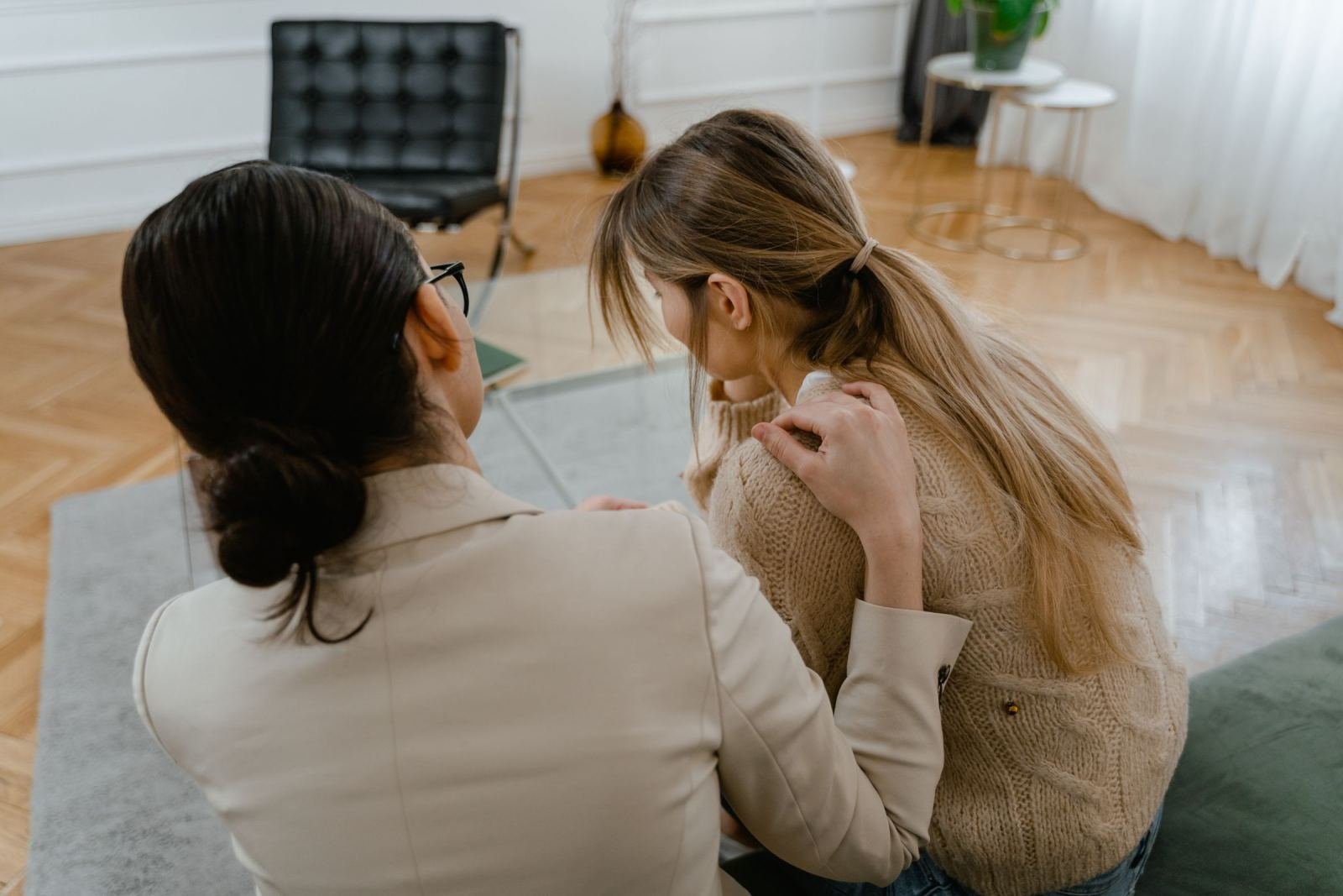A counselor places a supportive hand on a client's shoulder in an office
