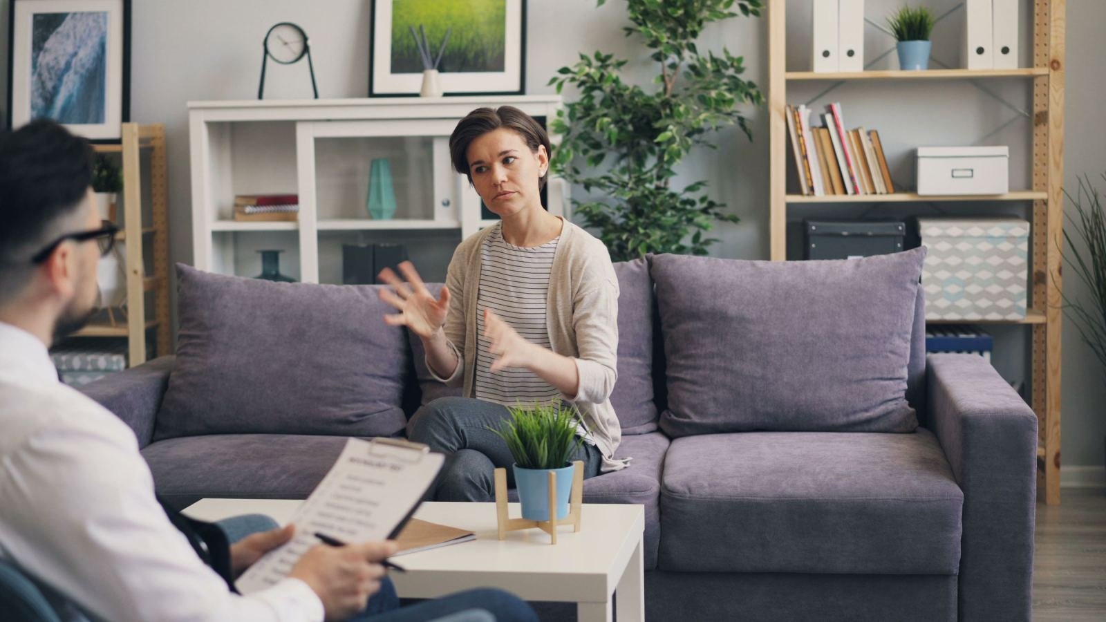 A woman gestures while speaking to a clinician holding a clipboard in an office