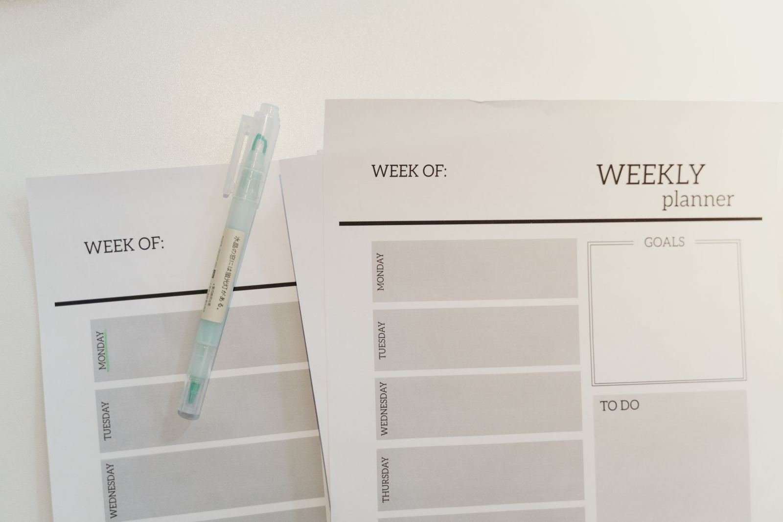 Two blank weekly planner pages and a pen on a white surface