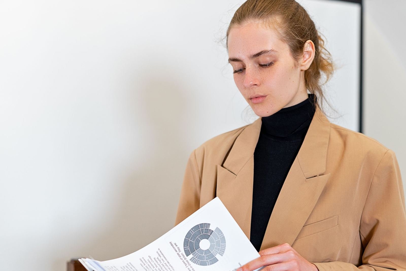 A woman in a tan blazer reviews a printed document with a circular chart