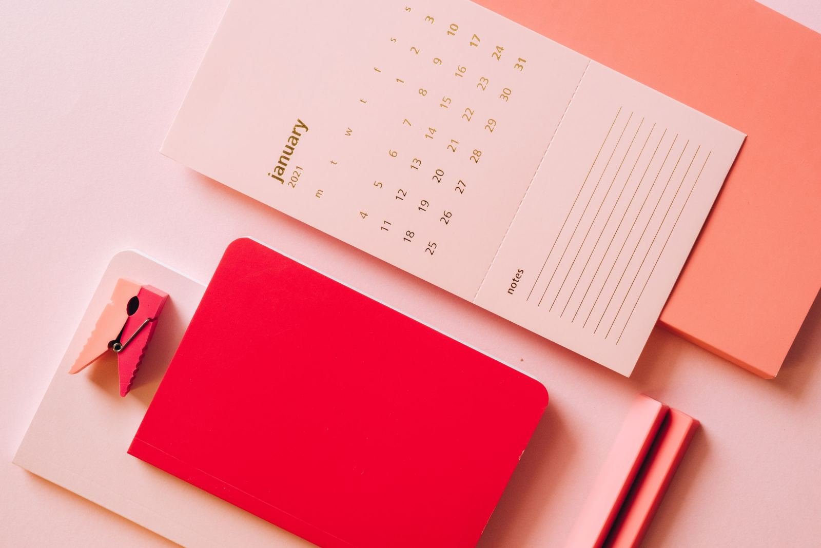 A January calendar, a red notebook, and a pink binder clip on a pink background