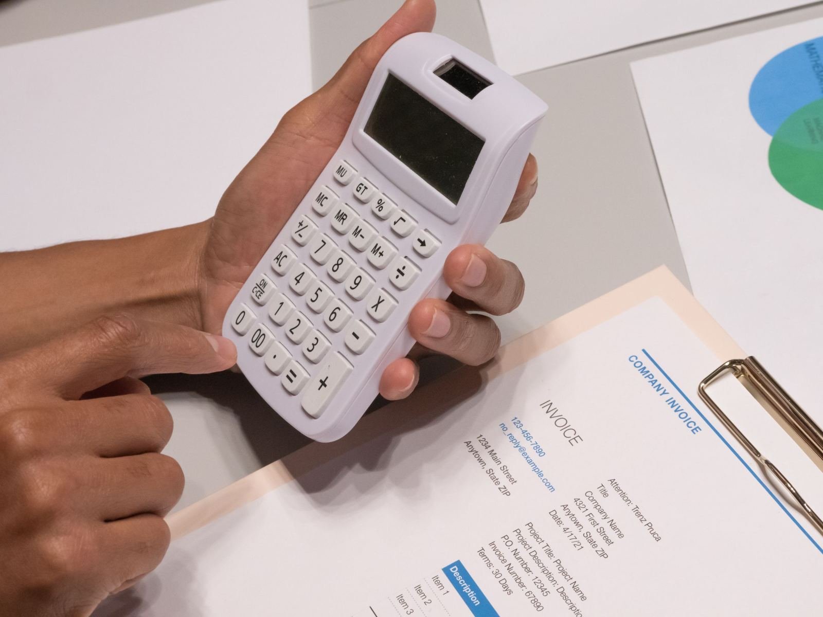 Hands using a white calculator over a printed invoice on a desk