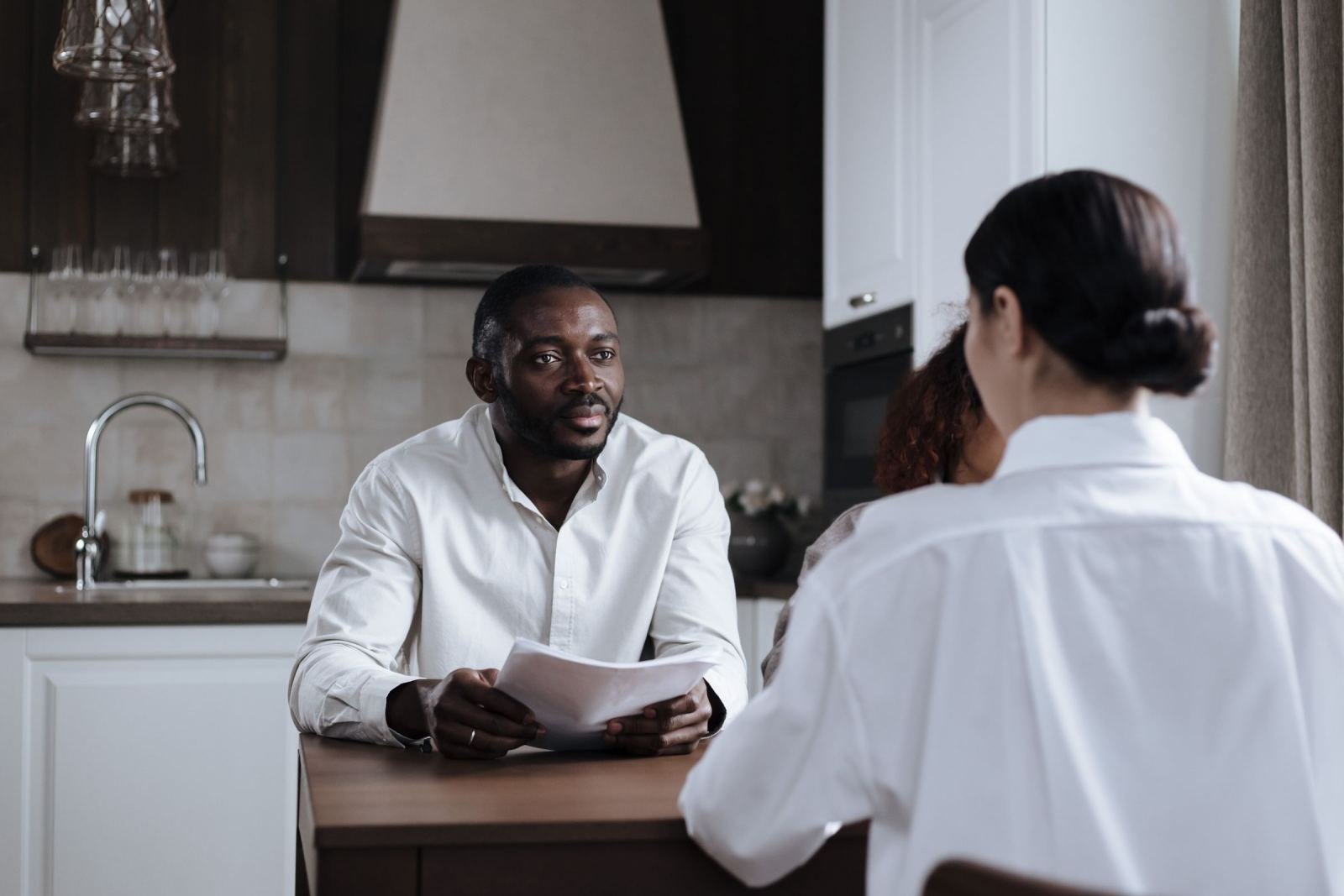 A man holding a piece of paper looks at a woman in a kitchen