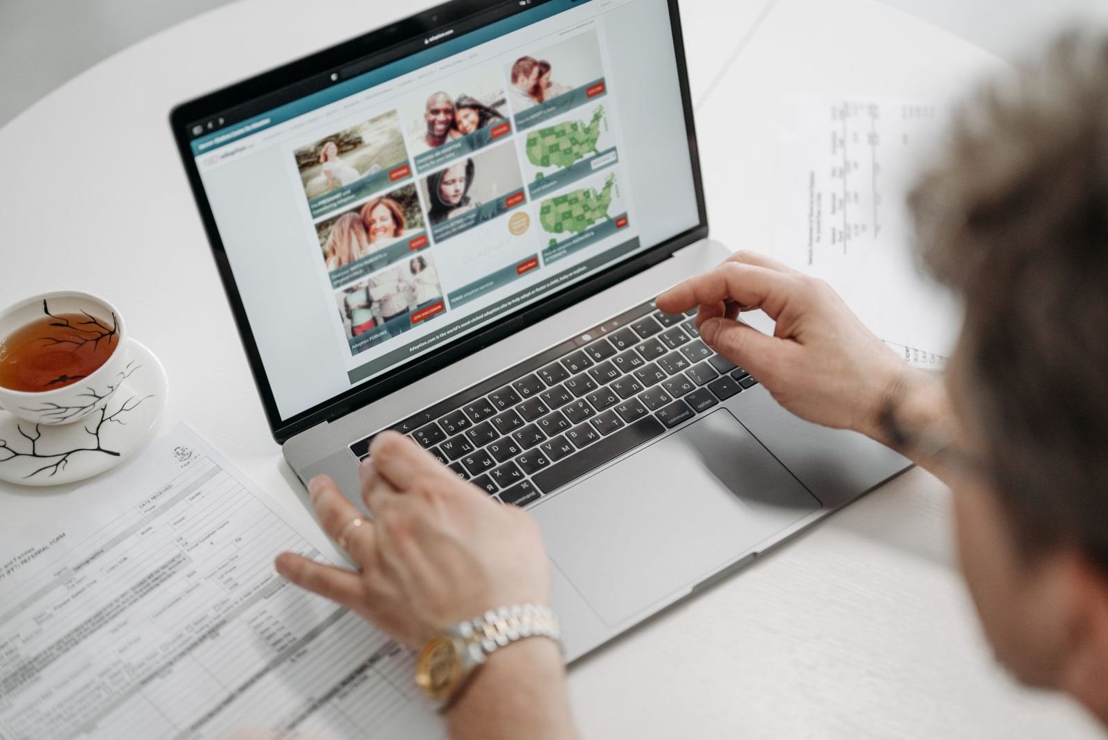 A person uses a laptop and reviews documents on a white table