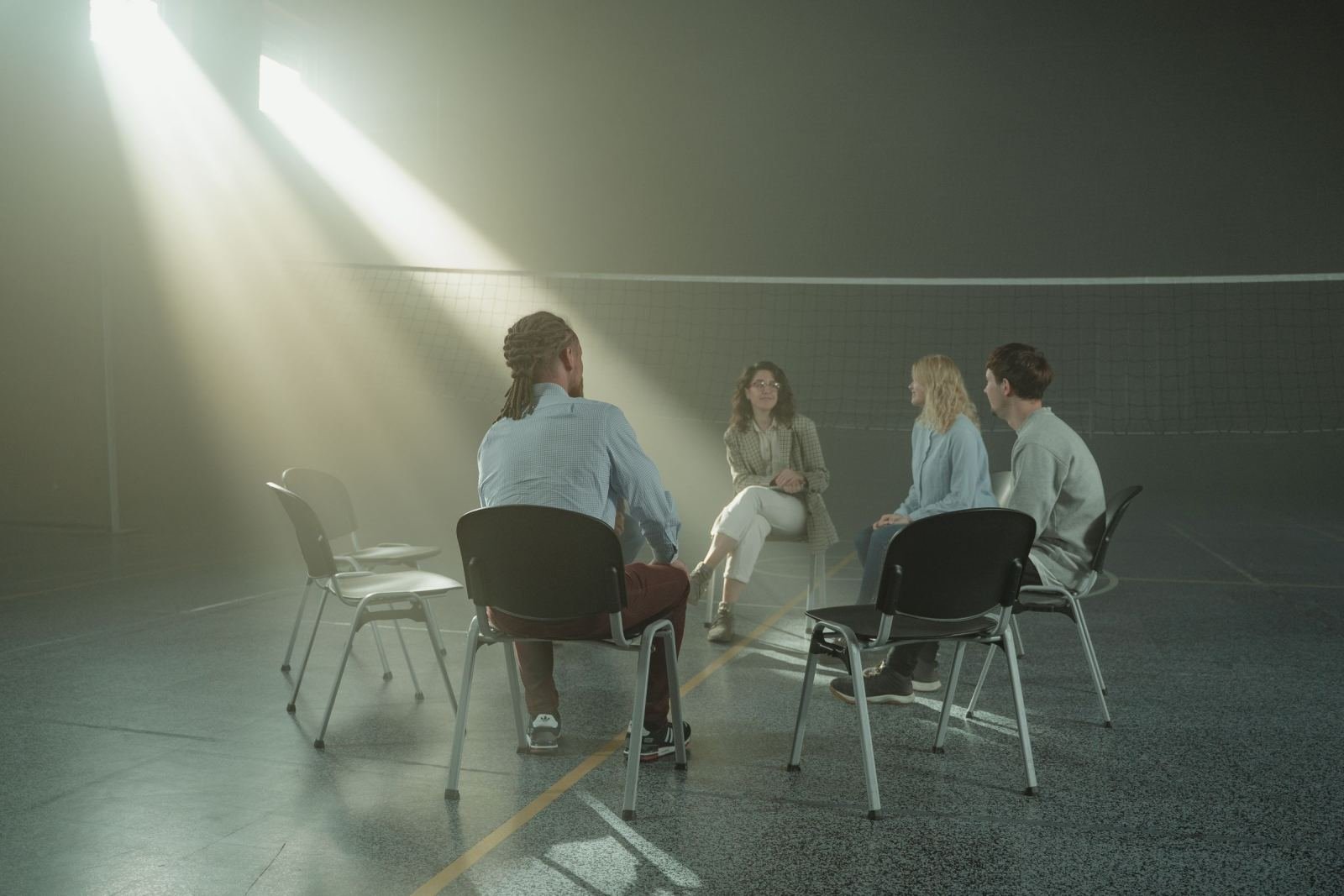 Four people sit in a circle of chairs in a large room with a beam of light shining down