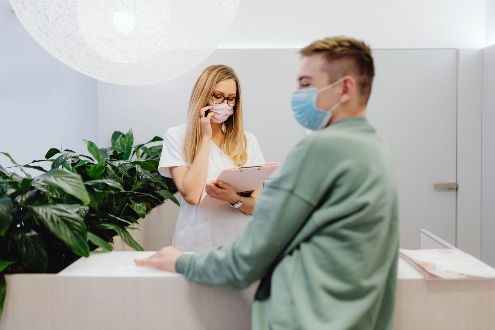 A clinic staff member with a clipboard speaks to a visitor at a reception desk