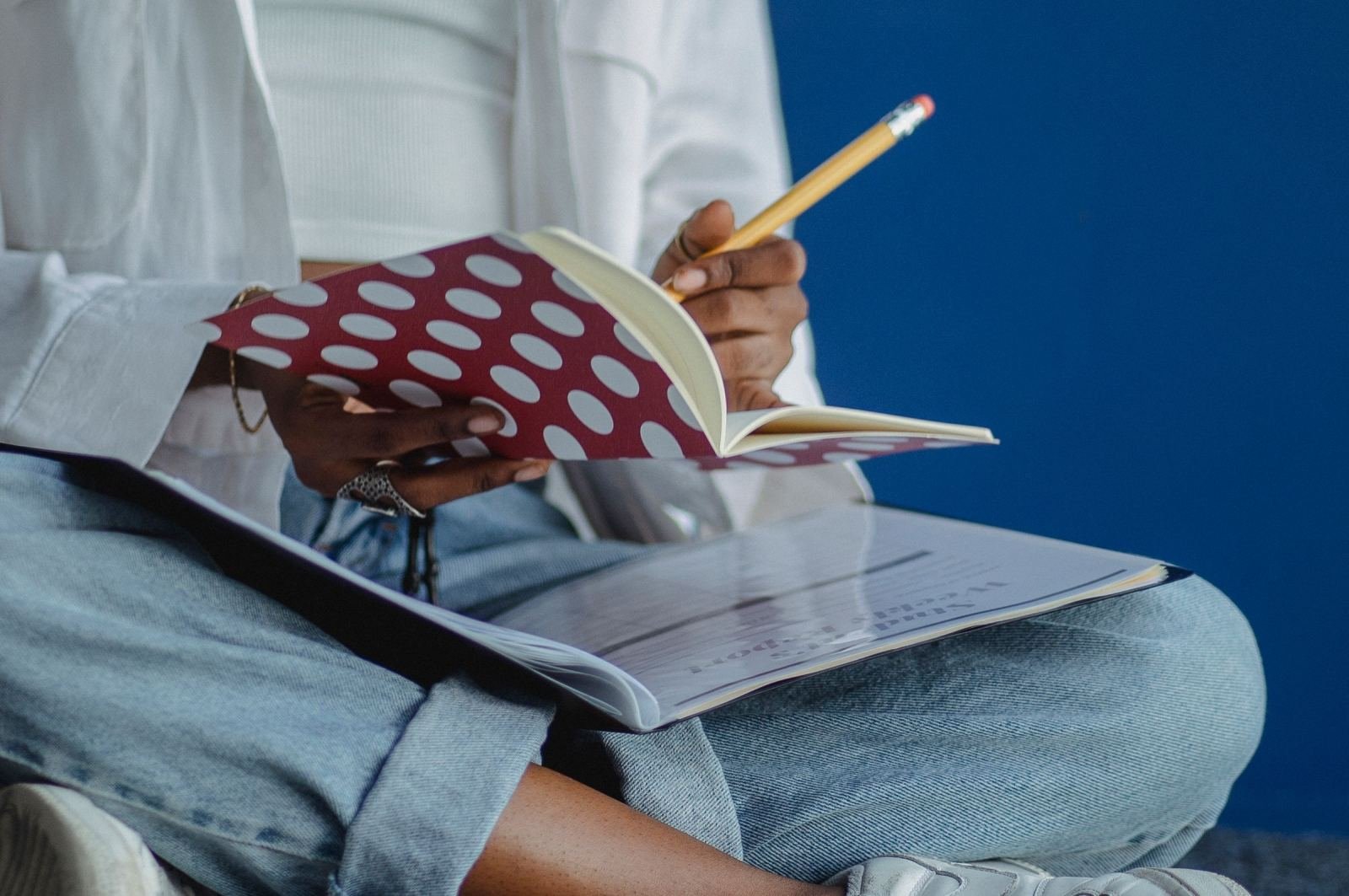 A person writing in a polka-dot notebook with a pencil while sitting with a binder on their lap