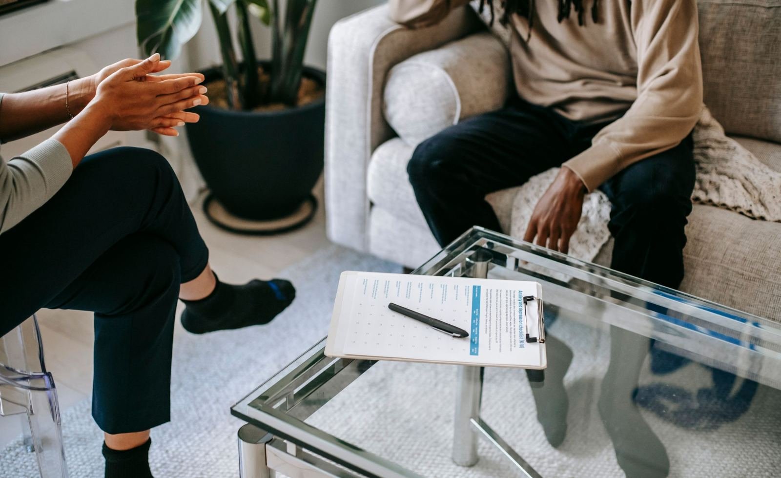 Two people sit across from each other with a clipboard on a glass table between them