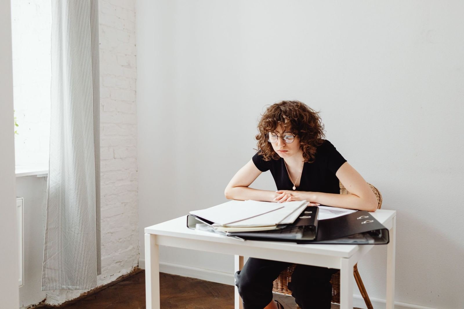 A woman with glasses reviews papers in a folder at a white table