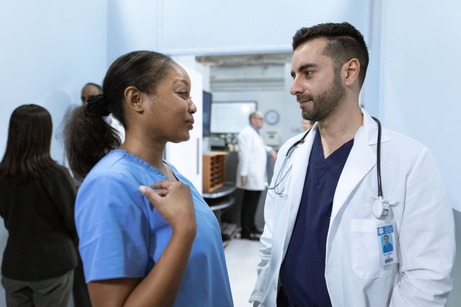 A doctor in a white coat and a nurse in blue scrubs talk in a bright clinic