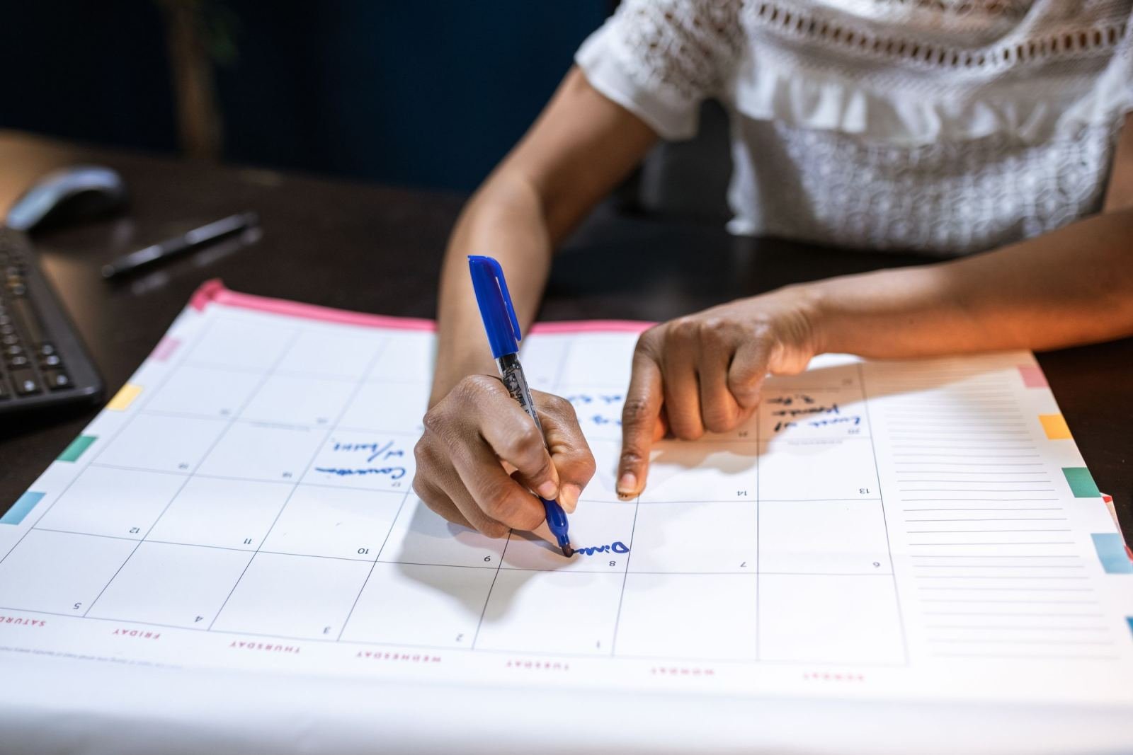 A person marks a date on a big paper calendar using a blue pen.