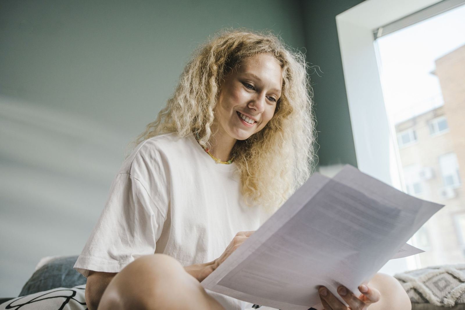A smiling woman with curly blonde hair reads a printed document