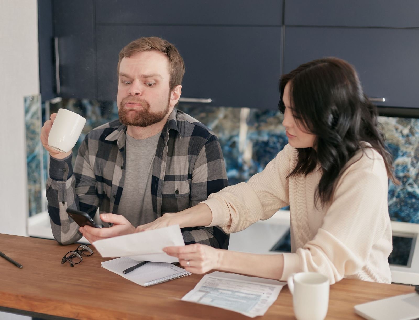 A man and woman sit at a table with a smartphone and paperwork