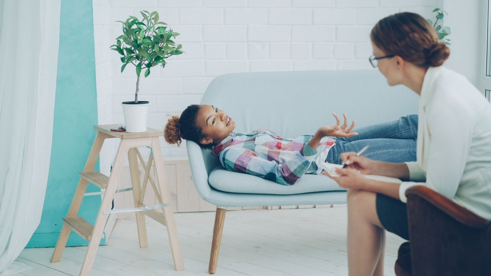 A woman lies on a sofa while talking to a counselor with a notebook